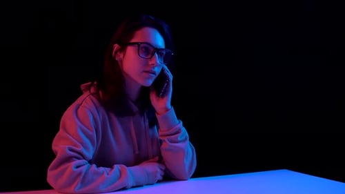 Junge Frau mit einem Telefon. Eine Frau telefoniert. Blaues und rotes Licht fällt auf eine Frau auf