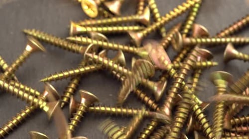 Pile of Shiny Gold Screws on Dark Surface
