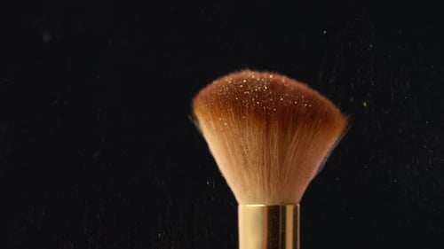 Sweeping Gold Shimmer Powder from Makeup Brush on Black Background