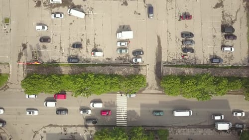 Vista aérea de cima para baixo da rua com carros em movimento e faixa de pedestres com pedestres cruzando.