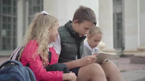 Positive Caucasian Schoolboy Resting with Classmates on School Stairs. Side View of Carefree Boy and