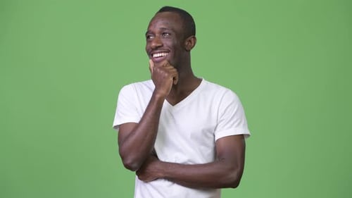 Junger glücklicher afrikanischer Mann denkt vor grünem Hintergrund