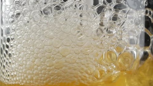 Nahaufnahme von Luftblasen, die von jemandem entstehen, der mit Stroh in ein volles Glas Bier oder Soda bläst