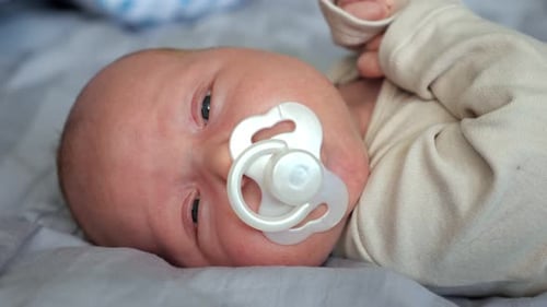 Adorable Newborn Baby Sucks Pacifier Lying in Bed at Home