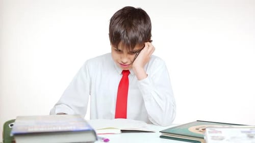 Young Caucasian School Kid in Red Tie Sitting at Table Writing Talking on Mobile Phone on White