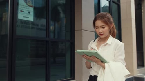 Businesswoman using digital tablet and typing text message while walking alone outdoor in city
