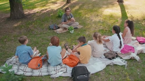 Teacher Showing Plant to Elementary School Children in Park