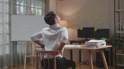 Back View Of Asian Man Having Backache While Working Hard With Documents At The Office