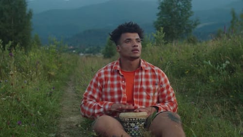 Handsome Hipster African Man Playing Djembe Drum on Mountain Hill at Sundown