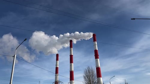 White smoke from the chimneys of an industrial plant against a blue sky.