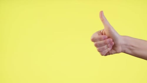 Close Up Cropped Man Hand Showing Thumb Up Gesture Sign Isolated on Yellow Background in Studio.