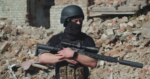 Un soldat ukrainien armé d'un fusil se tient debout sur le fond d'une maison détruite et regarde autour de lui