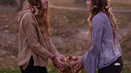 Two Friends Playfully Toss Leaves in Autumn