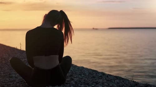 Woman Silhouetted Meditating on Beach at Sunset