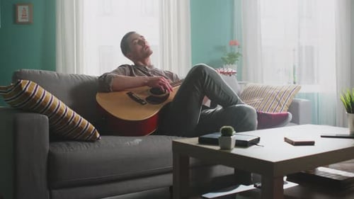 Man Playing Guitar Relaxing on Couch at Home