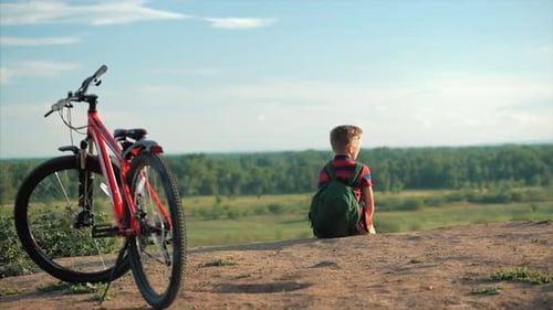 Teenager in a Red T-Shirt With a Backpack on His Back, at Sunset, Sitting on a High Hill