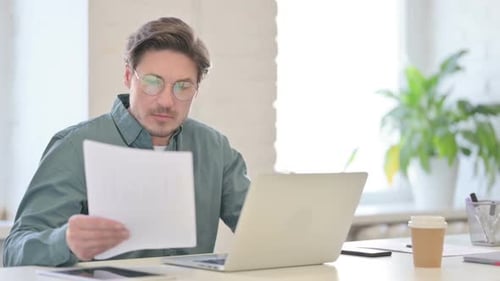 Man with Laptop Reading Documents in Office