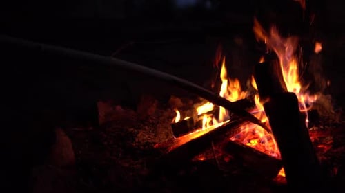 L'homme redresse les braises dans le feu. Le feu brûle au milieu de la nuit en gros plan.