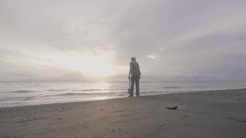 Middle Aged Man in Headphones with a Metal Detector Works on the Sea Sand Beach with His Dog at