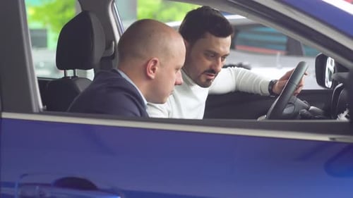Professional Salesman Smiling Showing a New Car at the Dealership to His Male Customer