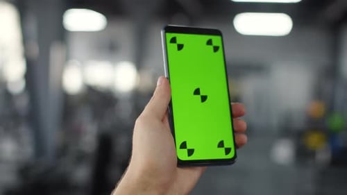 Man hand holds smartphone with chromakey in gym, closeup. Man hand holds smartphone with green scree