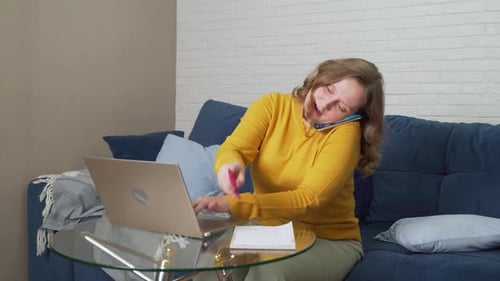 Woman Works at Laptop at Home and is in Hurry Writes Something and Talks on the Phone