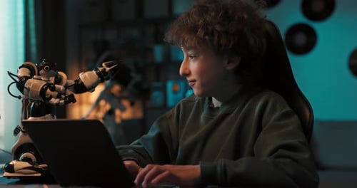 Young Talented Gifted Boy Sits in Room in the Dark and Programs a Robot on Laptop Adds New Features