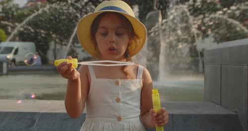 Cute Little Girl Blows Soap Bubbles on the Background of a Fountain
