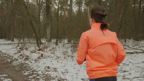 Woman Jogging Through Snowy Winter Forest Trail