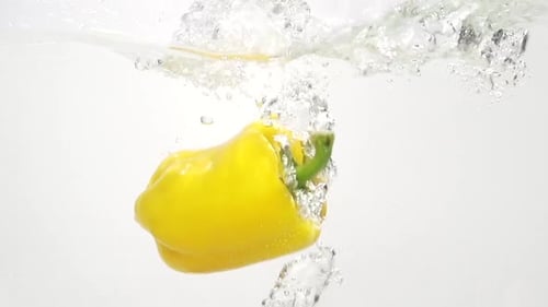 Gelber Pfeffer spritzt in Zeitlupe ins Wasser