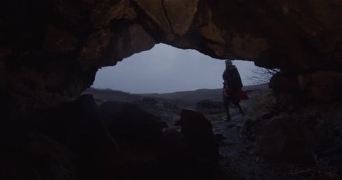 Woman Entering Fire Lit Cave At Dusk