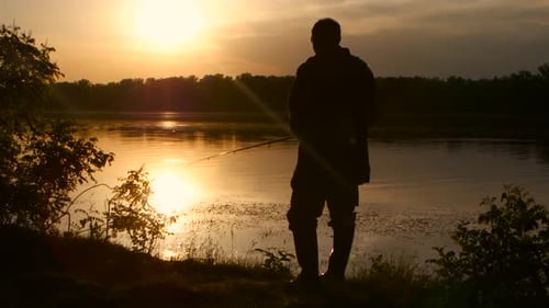 Silhouette Fisherman Casting at Lake During Golden Sunrise