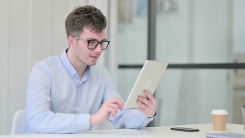 Excited Man Celebrates Success Using Tablet at Desk