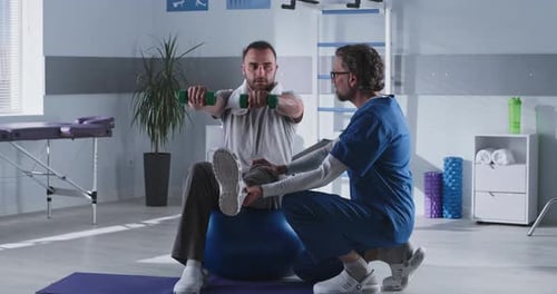Mature Therapist Supporting Male Patient on Fit Ball