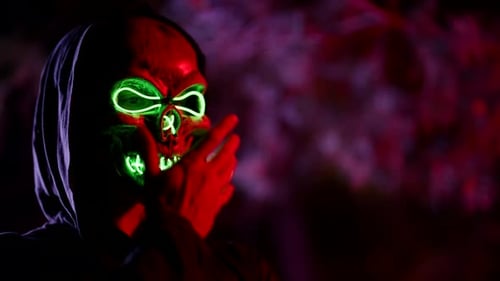 Hooded Person in Scary Neon Mask in the Dark