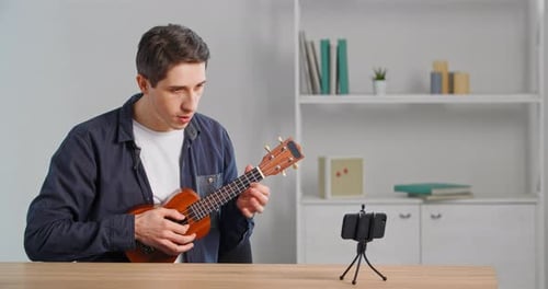 Man Playing Ukulele For Smartphone at a Desk