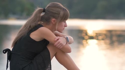 Young Woman Sitting by Lake during Sunset