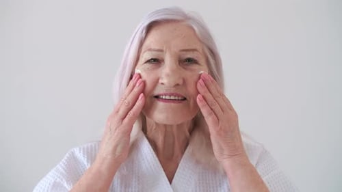 Senior Woman Applying Lotion to Face Smiling