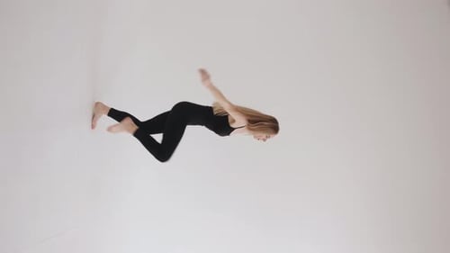 Charmantes junges Mädchen in einem schwarzen Oberteil und Leggings macht eine Ballett-Haltung Springen Sie im Studio auf einem