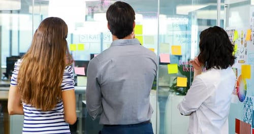 Coworkers Brainstorming Strategy on Glass Wall in Office