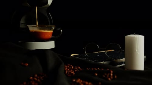 Coffee Dripping into Cup with Book and Candle