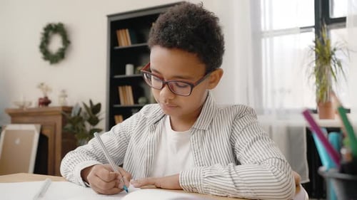 Boy Writes at Desk Indoors