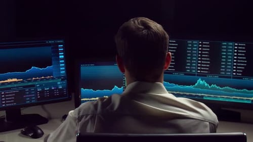 Comerciante que trabaja en la oficina de noche utilizando tecnología de estación de trabajo y análisis.