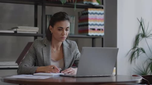 Woman Working at Laptop and Taking Notes Indoors