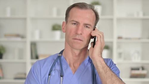 Male Doctor Talking on Smartphone in Hospital Office
