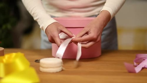 Woman Tying White Satin Ribbon on Pink Gift Box