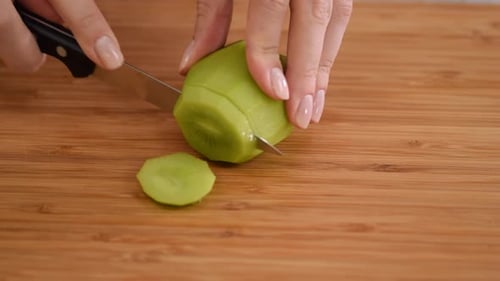Hands Slicing Fresh Kiwi Fruit on Cutting Board