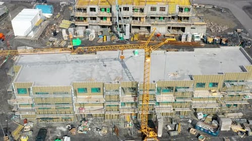 Vista aérea superior de una construcción de edificios, con una grúa torre instalada y coches estacionados durante el