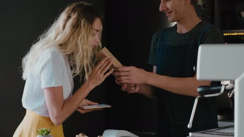 Smiling barista in a coffee shop putting beans in a craft bag and sells it for female customer