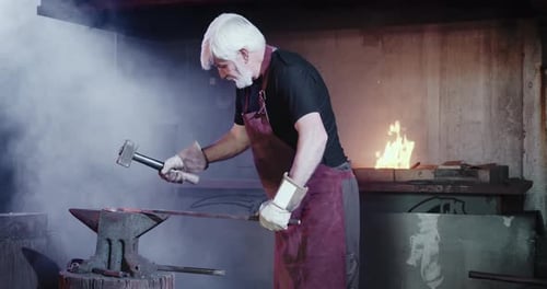 Senior Blacksmith Forging Metal in Smoky Workshop